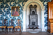 An antique cast iron stove, a portrait painting and chairs against a wall with blue patterned paper