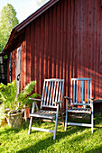 Zwei Holzstühle vor rot-braunem Holzhaus