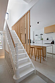 Treppenhaus mit weißen Treppen und offene Küche mit Kücheninsel, Holzsprossen als Raumteiler