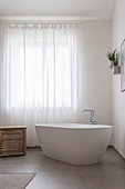 Frei stehende Badewanne vor Fenster mit Vorhang im Badezimmer
