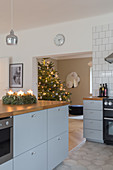 Adventskranz auf graublauer Kücheninsel mit Holzarbeitsplatte, im Hintergrund Weihnachtsbaum