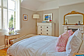 Double bed, white dresser and fireplace with mirror in the bedroom