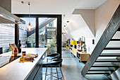 Island counter and bar stools next to metal stairs in loft apartment