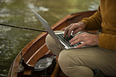 Man with laptop fly fishing in boat