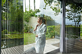 Woman in bathrobe looking out window