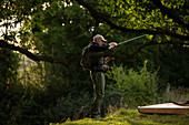 Man flying fishing under tree at riverbank