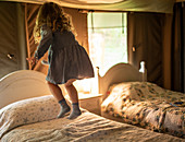 Happy girl in dress jumping on bed in cabin