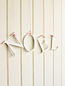 Decorative letters reading 'NOEL' hung from red and white strings on white wooden wall