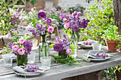 Spring bouquets of lilacs, roses, and allium with grass and a grass wreath as a table decoration, and a small clay pot with parsley