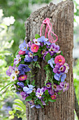 A small wreath of horned violets, daisies, and grass hung on a post