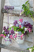 Small spring bouquets with lilacs and bleeding-hearts hung in cups on a wooden ladder