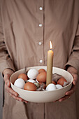 Bowl of white and brown eggs, feathers and a candle