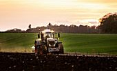 Ploughing a field at sunset with a tractor and plough, ready for crops on a farm