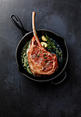 Raw fresh meat Tomahawk Steak in Cast iron frying pan on dark background