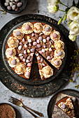 A partially sliced no-bake chocolate cheesecake decorated with whipped cream, chocolate flakes and candy Easter eggs