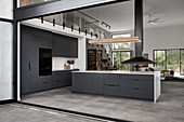 Black kitchen with island counter in open-plan interior with gallery level
