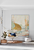 White swivel chair and pouffe below painting in corner