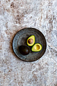 Avocado, sliced and whole on gray handmade ceramic plate