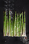 Raw green asparagus spears with sea salt and pepper on a dark background