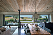 Wooden dining table in open-plan interior with sliding glass door and view of pool and countryside