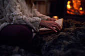 Woman reading book on blanket beside cosy fireside