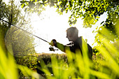 Man preparing fly fishing line under sunny tree