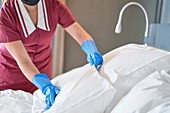 Hotel maid with gloves making bed in hotel room
