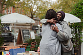 Happy mother and daughter hugging at cafe patio