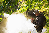 Man preparing fly fishing line at sunny riverbank