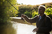 Man casting fly fishing pole at sunny river