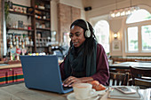 Woman with headphones working at laptop on cafe table