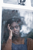 Sad young woman with head in hands looking out window