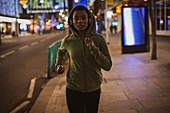 Young woman in hoody running on city sidewalk at night