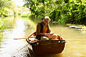 Man fly fishing and using smartphone in boat on river