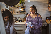 Mother and daughter drying dishes in apartment kitchen