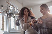 Happy mother and daughter using smartphone in kitchen