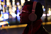 Young woman with headphones in city with lights at night