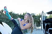 Happy young female surfer putting on wetsuit outside van