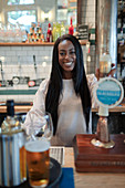 Happy young female bartender working behind bar