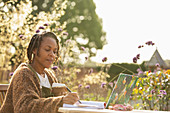 Woman with coffee working at laptop on sunny garden patio