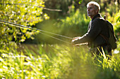 Man with backpack fly fishing with pole among grass