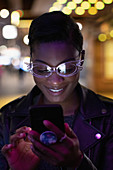 Young woman wearing glasses using smartphone at night