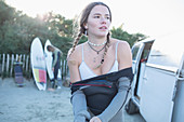 Young female surfer putting on wet suit outside camper van