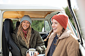 Happy young women friends with coffee in camper van doorway