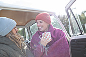 Happy young women friends drinking tea at sunny van doorway