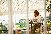 Female garden shop owner drinking tea at table in greenhouse