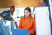 Young women friends with laptop and coffee inside camper van