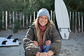 Happy young female surfer sitting on beach