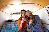 happy young women friends drinking tea in camper van