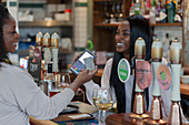 Customer paying female bartender with smart card in pub